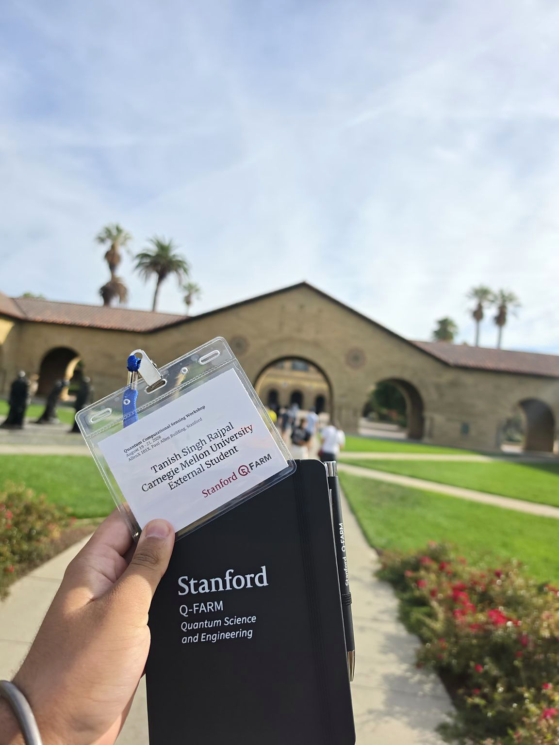 Stanford Q-FARM workshop badge and notebook held in front of the Stanford campus