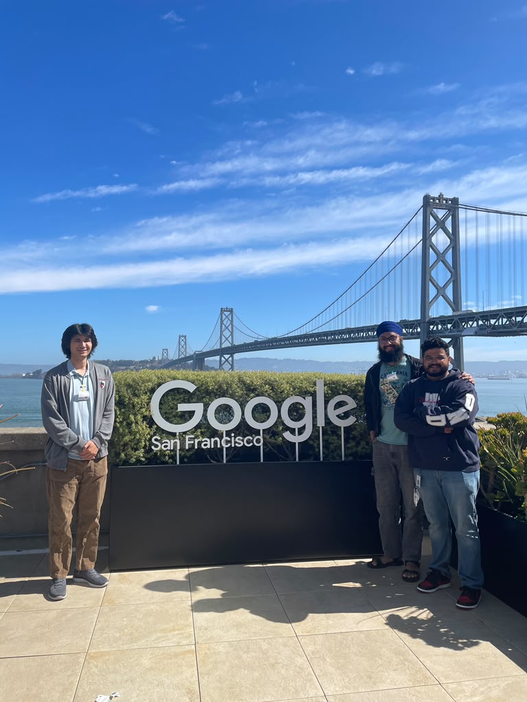 Tanish Singh Rajpal and two companions beside the Google San Francisco sign with the Bay Bridge behind them