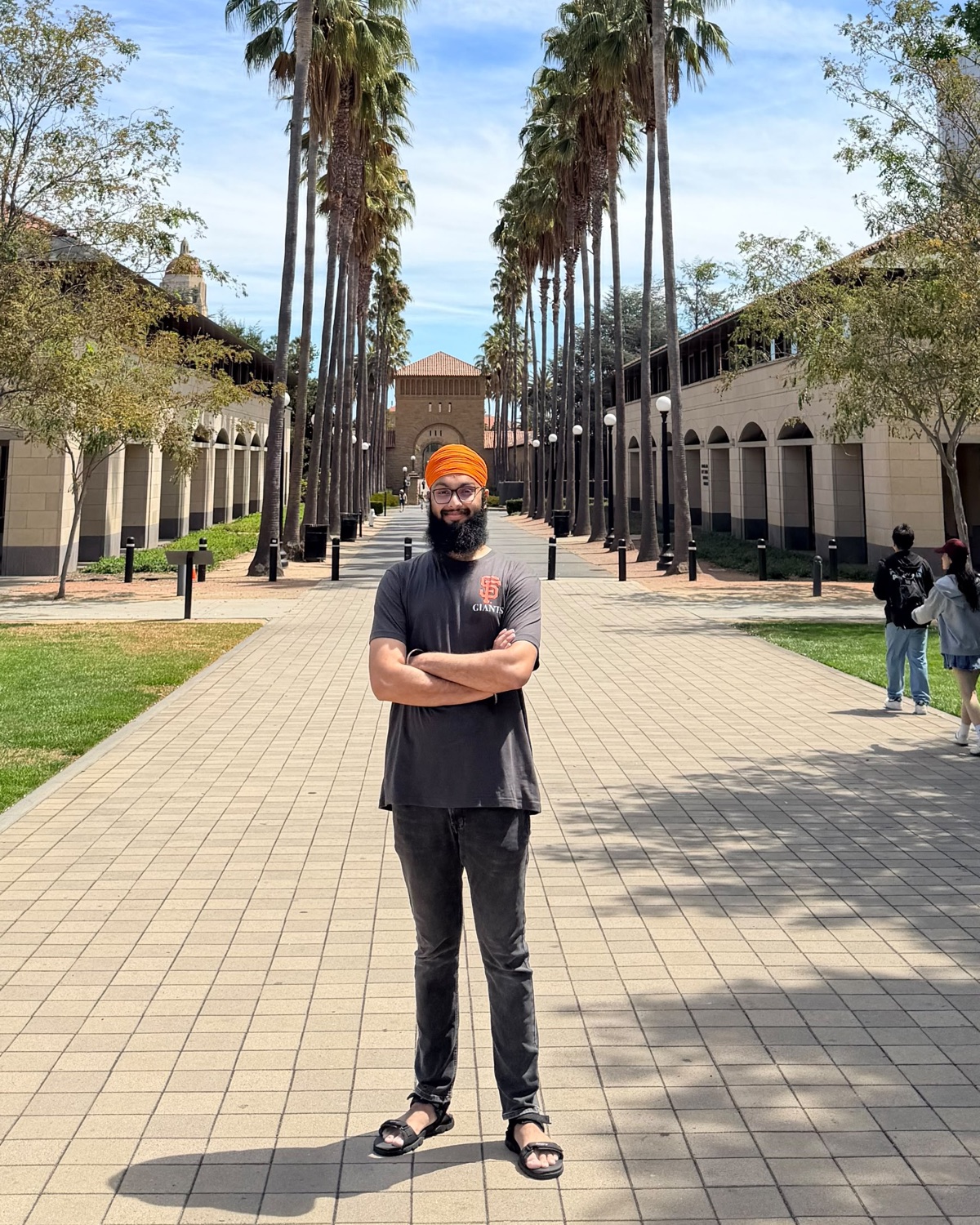 Tanish Singh Rajpal standing on a palm-lined campus walkway during a visit to Stanford University